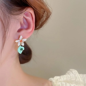 Detail shot of asymmetric floral bow earrings with colorful enamel and gemstones on model