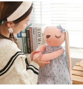 Close-up of pink long-eared bunny plush toy wearing a blue leaf pattern dress