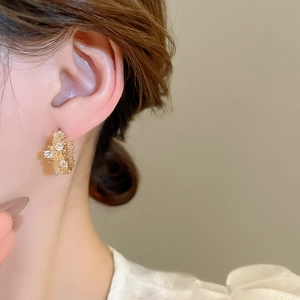 Close-up of golden C-shaped zircon earrings with textured finish and sparkling stones