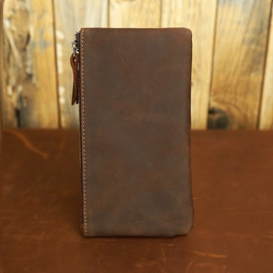 Vertical detail of dark brown crazy horse leather long wallet with zipper on rustic wood