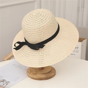 Dettaglio di un cappello di paglia beige con nastro nero su un supporto in legno