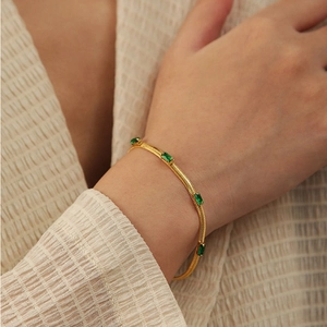 Detail of gold snake chain bracelet featuring emerald green rectangular zircon stones