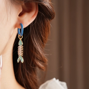 Close-up of a blue titanium hoop earring with a mint green enamel fishbone charm