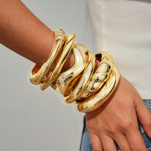 Detail of stacked chunky gold irregular geometric bracelets on a female model