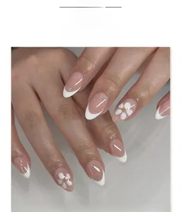 Dettaglio di unghie finte French con fiori 3D bianchi e decorazioni in perle dorate
