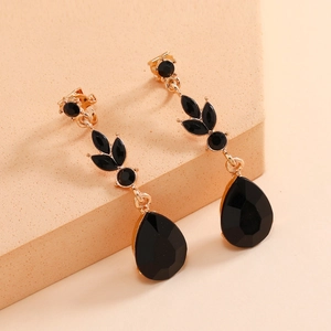 Elegant gold drop earrings with black teardrop gemstones on a minimalist geometric block