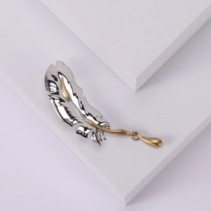 Elegant feather brooch in silver and gold metal finish displayed on white background