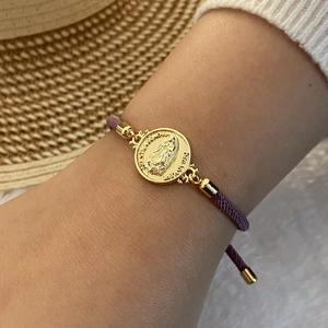 Detailed macro of a purple braided bracelet featuring a gold Virgin Mary charm