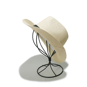 Close-up of beige woven straw hat with black ribbon detail on a metal display stand