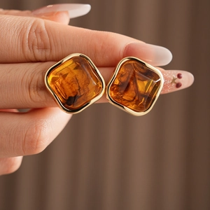 Macro detail of amber resin earrings with gold metal frame shown on model's ear