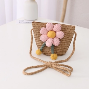 Detail of a children's straw crossbody bag with pink fabric flower and soft pom-poms