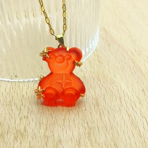 Close-up of orange resin bear pendant with gold star motifs on a thin gold chain
