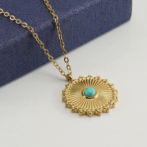 Close-up of 18k gold pendant necklace with sunburst texture and turquoise center