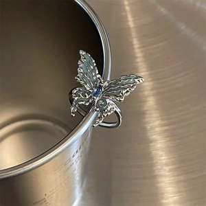 Macro detail of silver butterfly ring with teal enamel and blue gem on metal cup edge