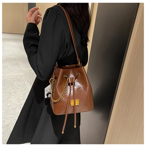 Détail du sac seau en cuir marron foncé avec chaîne dorée et breloque 8-ball sur modèle