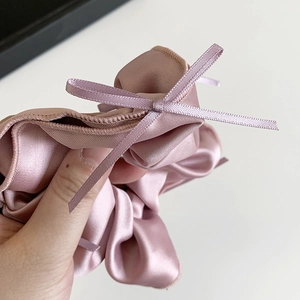 Pink purple satin scrunchie with delicate ribbon bows shown in a close-up hand shot