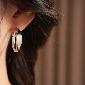Close-up of minimalist wide silver hoop earring on ear with smooth polished finish