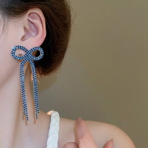 Close-up of model wearing blue rhinestone bow tassel earrings with sparkling crystals
