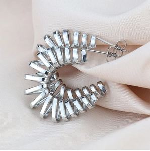 Macro detail of silver-toned spiral C-shape hoop earring on champagne silk fabric