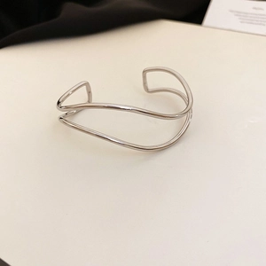 Close-up of minimalist silver cross wave bangle with polished metal finish