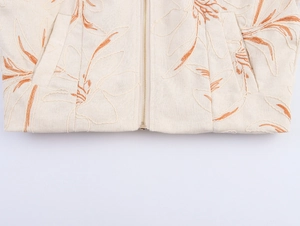 Detail of embroidered plant pattern and metal zipper on beige linen jacket