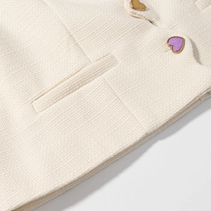 Dettaglio del tessuto tweed bianco crema con bottoni a cuore e tasca rifinita