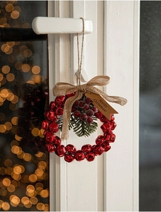 Red Christmas bell wreath decoration with pine needles and burlap bow on door handle