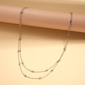 Detail of silver double-layered beaded chain necklace with oval metal beads on a soft backdrop