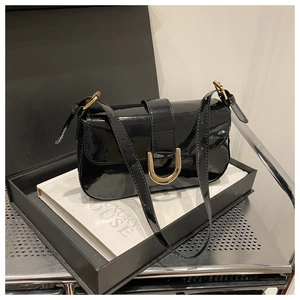 Close-up of black patent leather shoulder bag with gold horseshoe buckle in a luxury gift box
