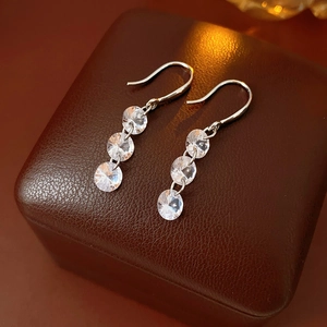 Detail view of silver drop earrings with three round cubic zirconia on a brown leather box