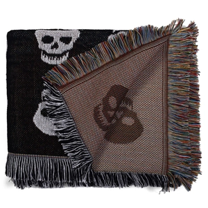 Close-up of bohemian woven blanket featuring a white skull pattern and colorful fringe