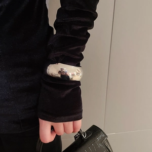 Polished silver wide oval open bangle displayed on a black sleeve with luxury handbag