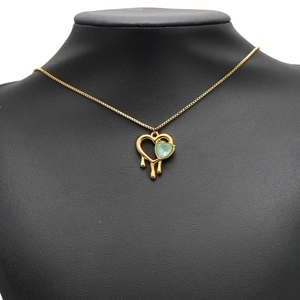 Gold melting heart necklace with green gemstone pendant displayed on a black neck bust
