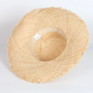 Detailed macro view of 100% natural raffia straw weave and fringed edge brim on summer hat