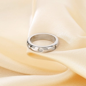 Macro shot of silver stainless steel ring with three inlaid diamonds on satin fabric