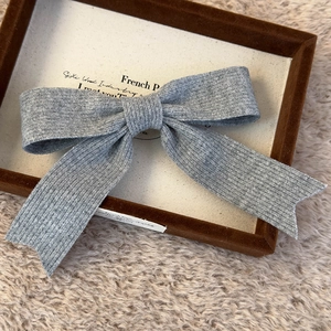 Detail shot of the gray knitted bow hair clip on a premium velvet jewelry display tray