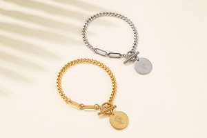 Detail of gold and silver chain bracelets with coin pendants and toggle clasps on beige background
