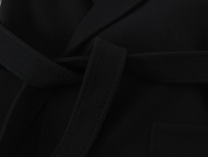 Close-up detail of a black woolen coat featuring a waist tie belt and fine stitching
