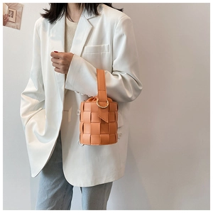 Detail of orange woven leather bucket bag with ring handle held by model in white suit