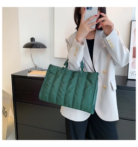 Detail shot of the dark green quilted nylon tote bag worn by a model in a modern setting