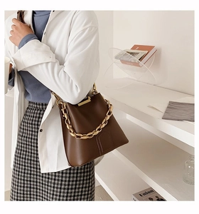 Detail of a large brown leather bucket bag with a bold gold chain handle worn by a model