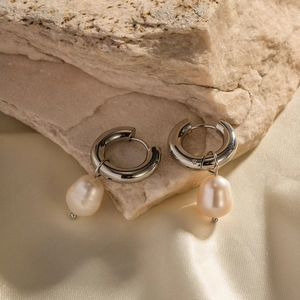 Macro view of teardrop pearl earrings with silver rings on rough stone and satin fabric
