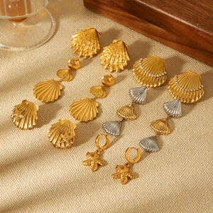 Detailed arrangement of 18k gold starfish and shell earrings on a soft beige fabric background