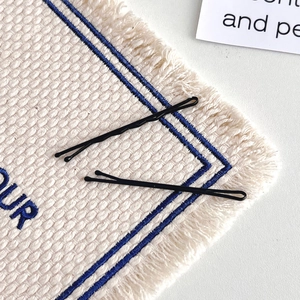 Close-up of black matte finish bobby pins in wavy and straight styles on a fabric background