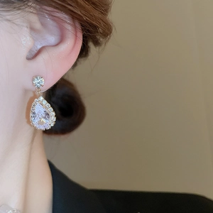 Close-up of golden teardrop earring with transparent crystal and shimmering pavé diamonds
