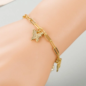Close-up of a gold paperclip link bracelet with a sparkling butterfly charm on wrist