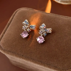 Detail of gold bow earrings with colorful rhinestones and a large pink crystal drop