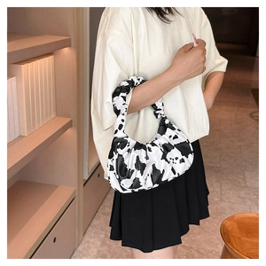 Detail of cow print pleated cloud bag worn by a model in a casual indoor setting