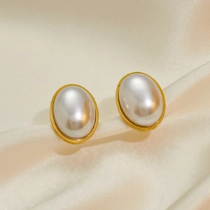Macro shot of oval pearl earrings with gold frames on smooth beige silk fabric
