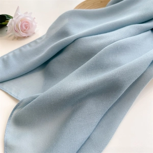 Detail shot of light blue cotton linen scarf with soft texture and natural folds on white